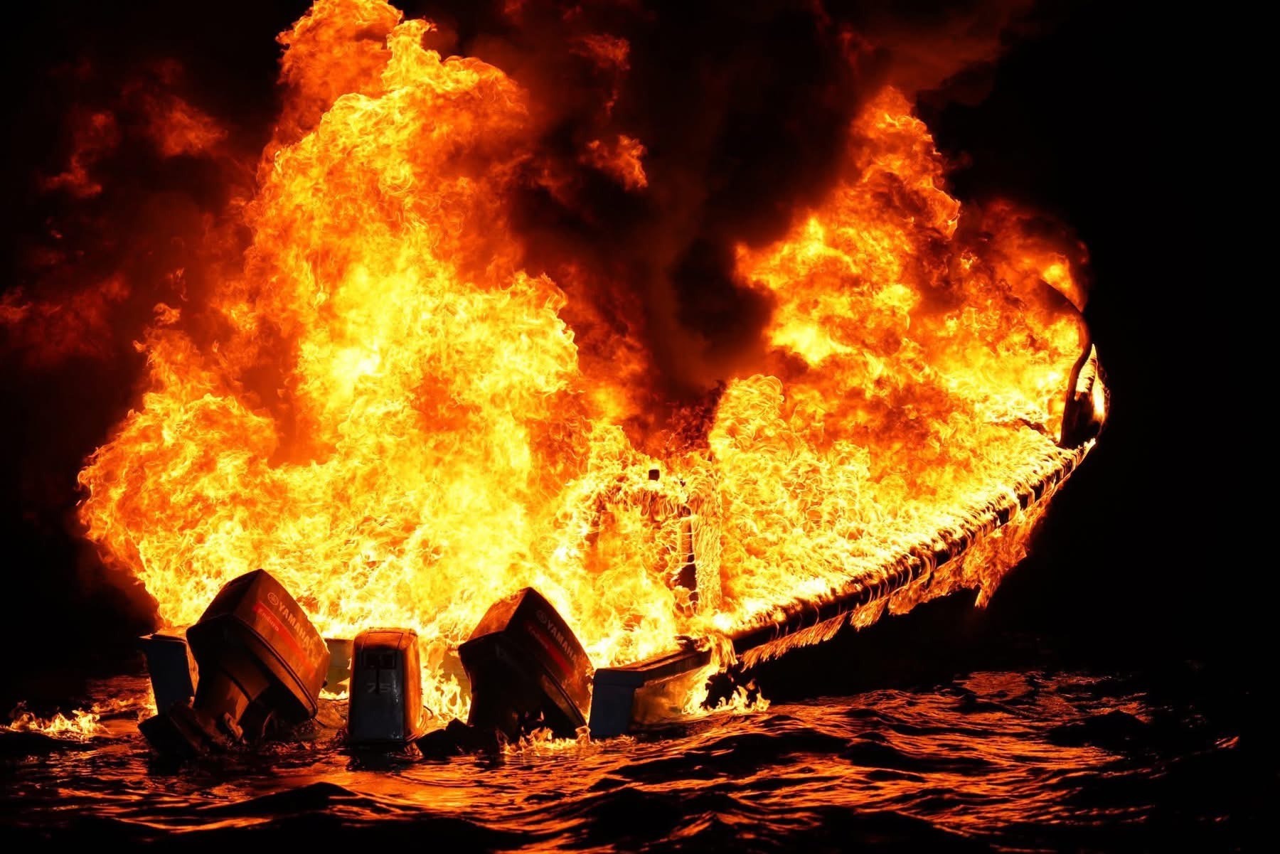 A burning boat on dark water